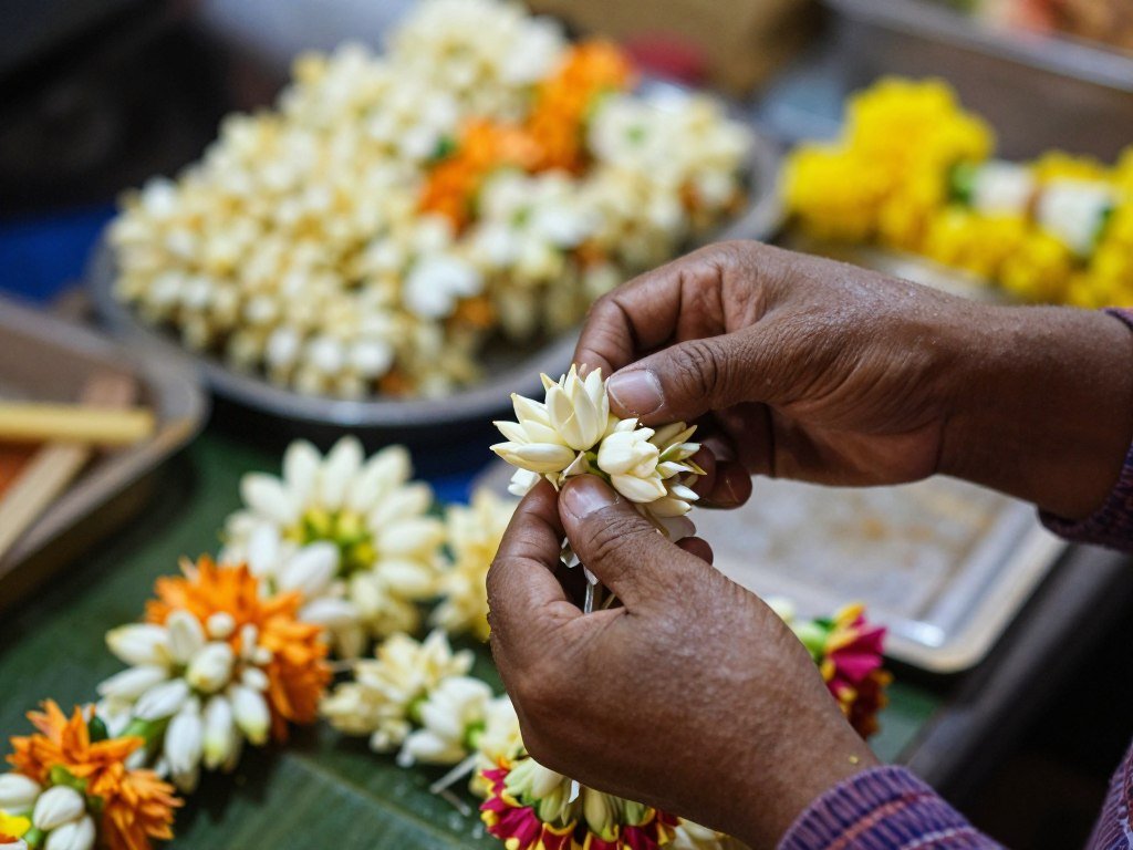 Close up of vendor hands arranging traditional Thai flower garlands at wholesale market